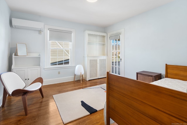 bedroom featuring an AC wall unit, wood finished floors, and baseboards