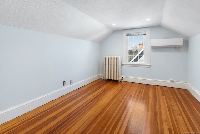 bonus room featuring a textured ceiling, baseboards, a wall mounted AC, radiator, and hardwood / wood-style floors