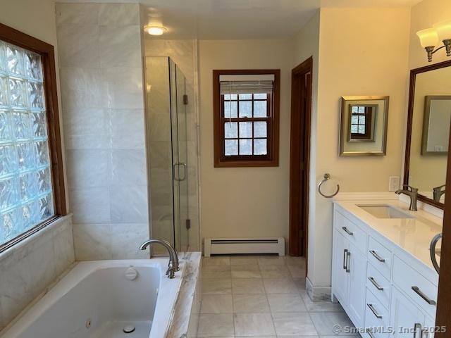 bathroom with a tub with jets, a stall shower, baseboard heating, and a sink