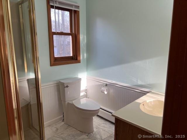 bathroom featuring a baseboard radiator, toilet, marble finish floor, and a wainscoted wall