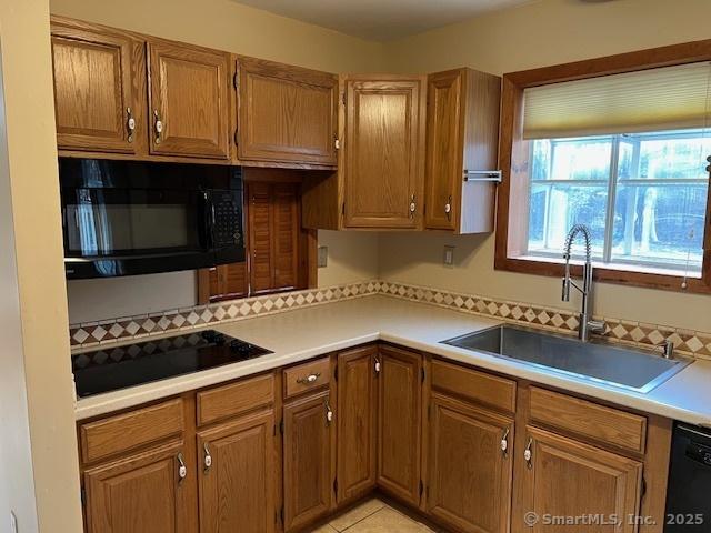 kitchen with black appliances, brown cabinetry, light countertops, and a sink