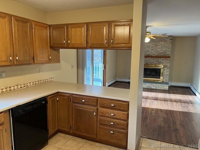 kitchen featuring brown cabinetry, a ceiling fan, light countertops, dishwasher, and a brick fireplace