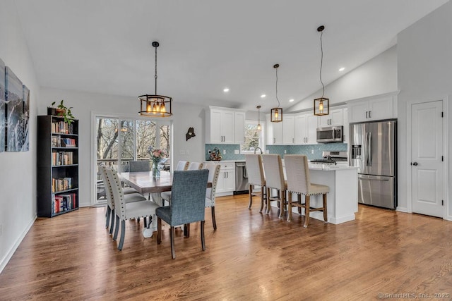 dining space with an inviting chandelier, recessed lighting, wood finished floors, and high vaulted ceiling