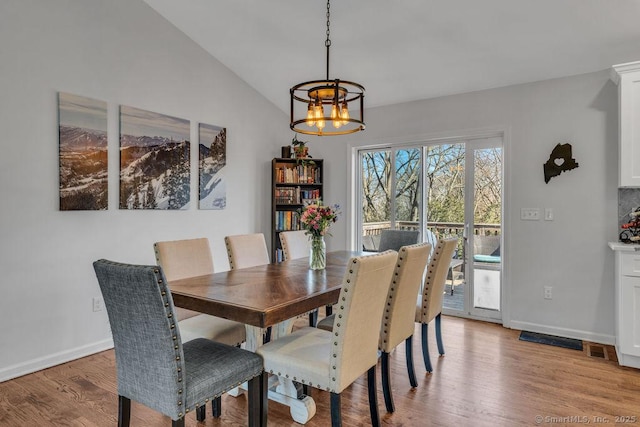 dining space with visible vents, baseboards, lofted ceiling, light wood-style flooring, and a chandelier