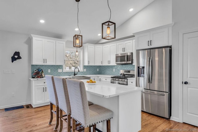 kitchen with a sink, appliances with stainless steel finishes, white cabinets, and vaulted ceiling