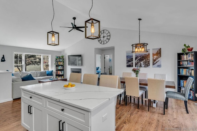 kitchen with lofted ceiling, a fireplace, white cabinets, light wood-style floors, and pendant lighting