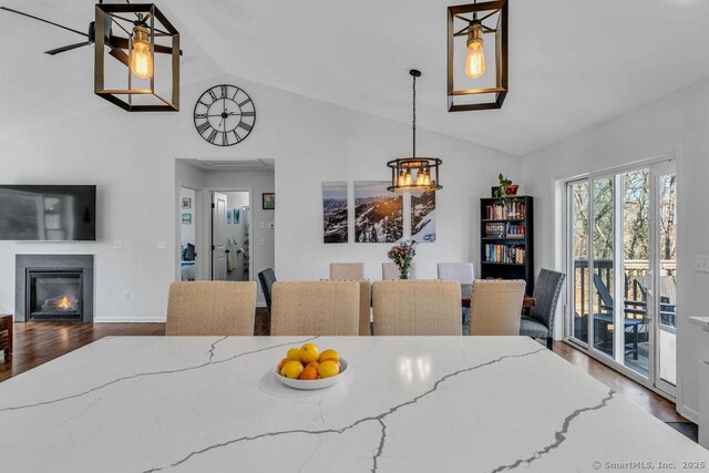 dining area with a glass covered fireplace, lofted ceiling, wood finished floors, and baseboards