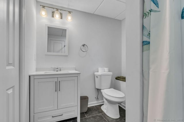 full bath featuring tile patterned flooring, baseboards, a drop ceiling, toilet, and vanity