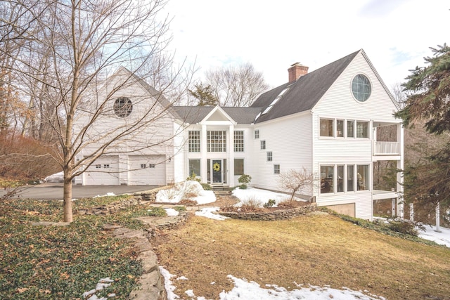 rear view of property with a garage, a chimney, aphalt driveway, and a yard