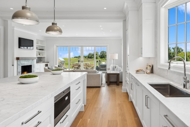 kitchen featuring stainless steel microwave, open floor plan, white cabinetry, a sink, and light wood-type flooring