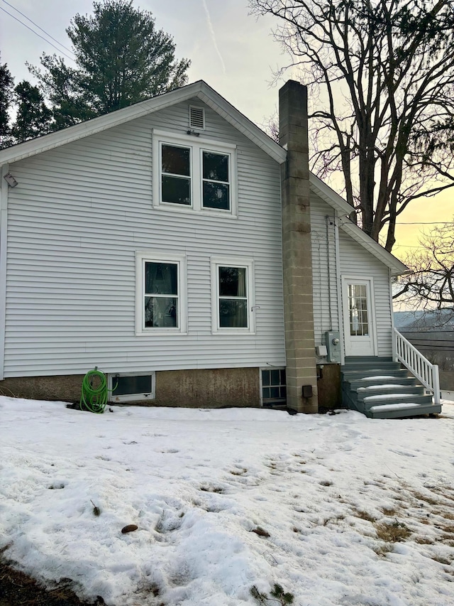 snow covered back of property with entry steps and a chimney