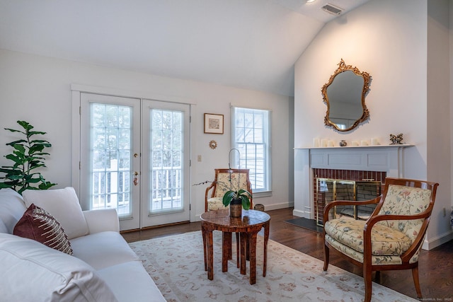 living room with visible vents, wood finished floors, french doors, lofted ceiling, and a brick fireplace