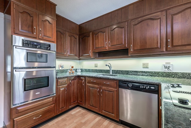 kitchen featuring dark stone counters, light wood-style flooring, appliances with stainless steel finishes, a textured ceiling, and a sink