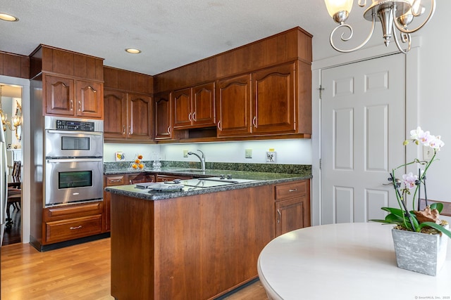 kitchen with light wood-style flooring, a textured ceiling, stainless steel double oven, a peninsula, and a chandelier