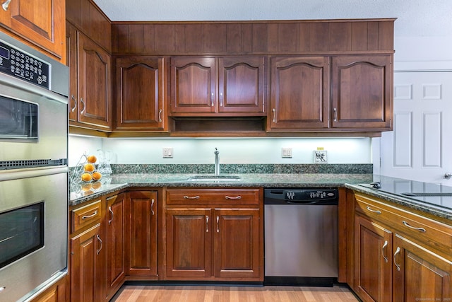 kitchen featuring dark stone countertops, light wood finished floors, a sink, stainless steel appliances, and a textured ceiling