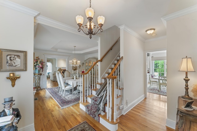 staircase featuring crown molding, a notable chandelier, baseboards, and wood finished floors