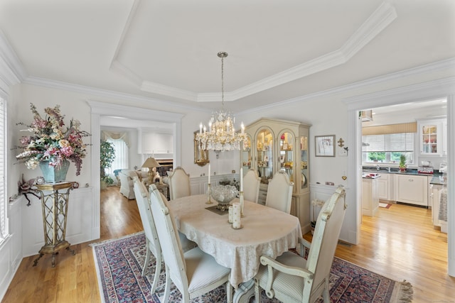 dining space with a chandelier, a tray ceiling, ornamental molding, and light wood-style floors