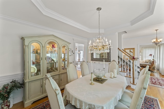 dining room featuring a raised ceiling, wood finished floors, stairs, crown molding, and a notable chandelier