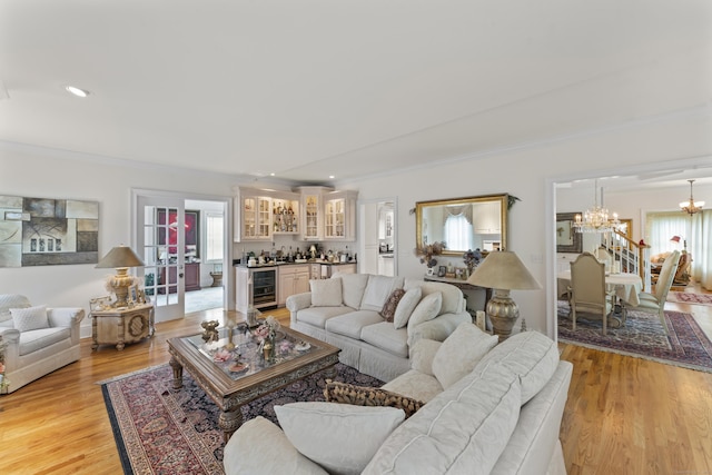 living room featuring crown molding, light wood finished floors, a dry bar, an inviting chandelier, and beverage cooler