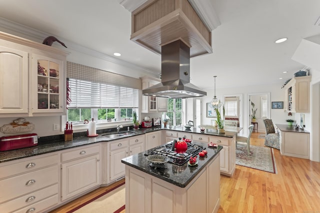 kitchen with glass insert cabinets, a sink, gas cooktop, island range hood, and a peninsula