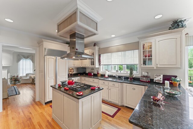 kitchen featuring crown molding, glass insert cabinets, a sink, gas cooktop, and island range hood