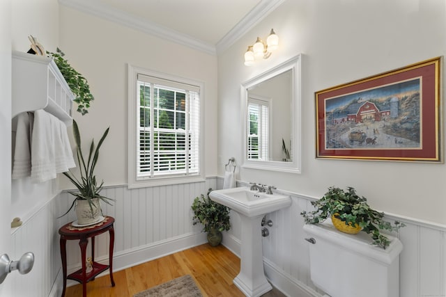 bathroom featuring toilet, ornamental molding, wood finished floors, and wainscoting