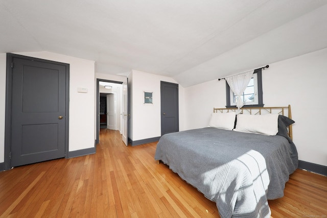 bedroom featuring lofted ceiling, a closet, light wood-style flooring, and baseboards