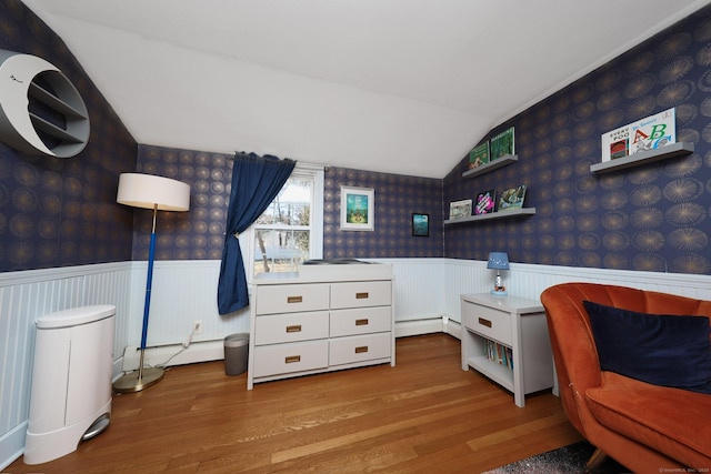 bedroom with lofted ceiling, wood finished floors, baseboard heating, wainscoting, and wallpapered walls