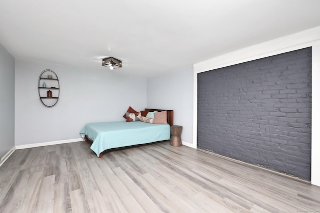 unfurnished bedroom featuring brick wall, wood finished floors, and baseboards