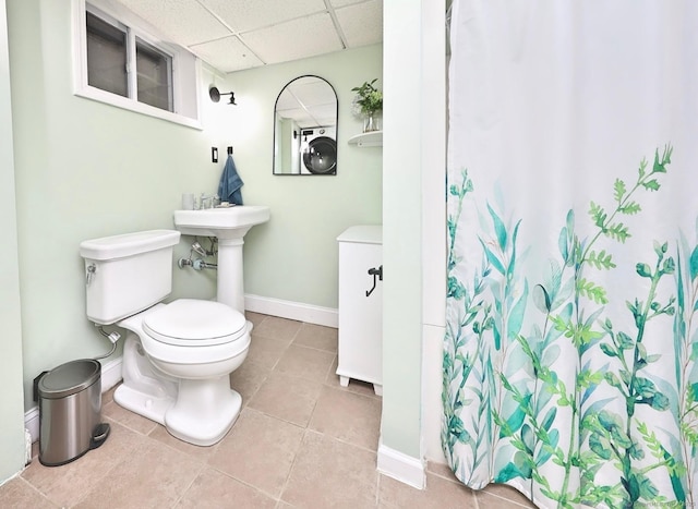 bathroom featuring baseboards, a drop ceiling, toilet, tile patterned floors, and curtained shower