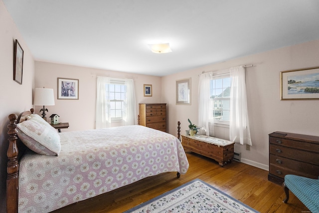 bedroom featuring a baseboard radiator, multiple windows, baseboards, and wood finished floors