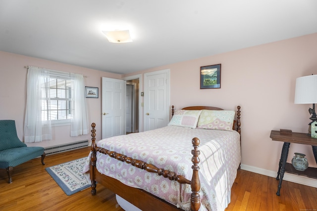 bedroom featuring a baseboard heating unit, wood finished floors, and baseboards