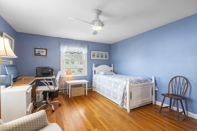 bedroom featuring baseboard heating, wood finished floors, a ceiling fan, and baseboards