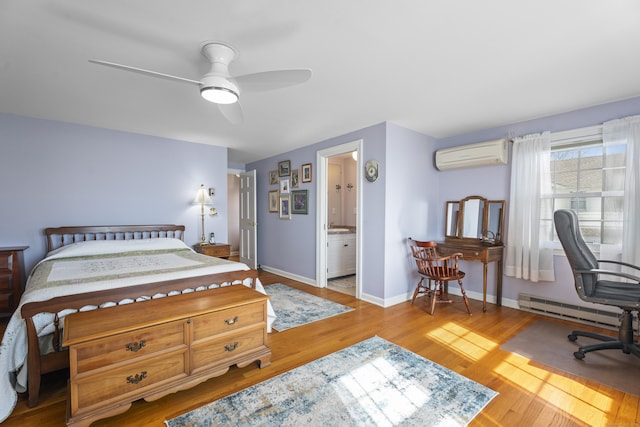 bedroom featuring baseboard heating, ensuite bathroom, an AC wall unit, wood finished floors, and baseboards