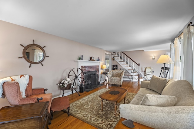 living area featuring stairs, a brick fireplace, and wood finished floors