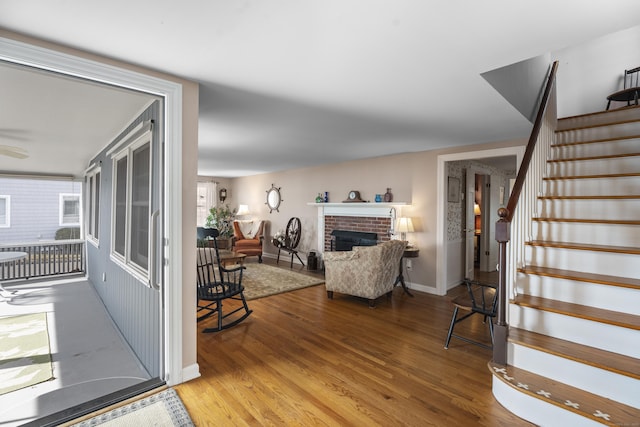 living room featuring stairs, a fireplace, baseboards, and wood finished floors