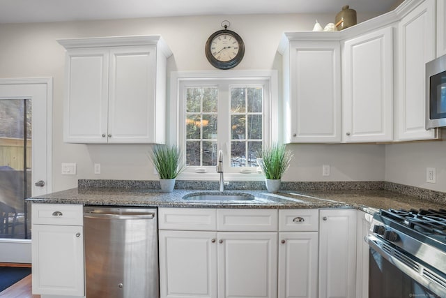 kitchen featuring stainless steel appliances, white cabinets, a sink, and dark stone countertops