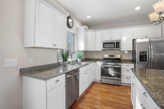 kitchen featuring a sink, white cabinetry, appliances with stainless steel finishes, light wood finished floors, and dark stone countertops