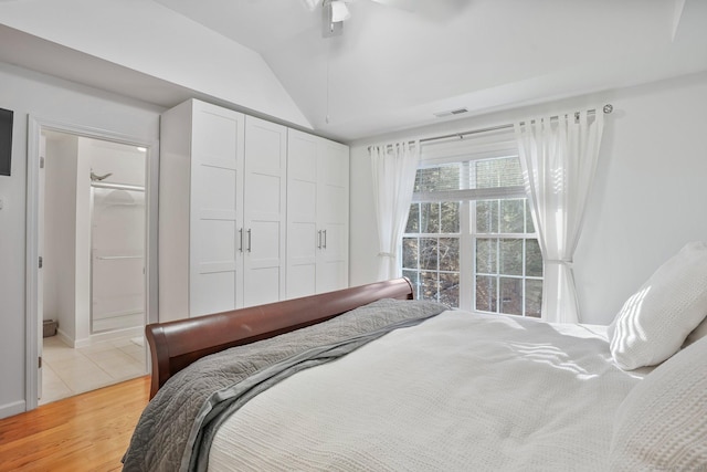 bedroom with a closet, visible vents, ensuite bathroom, vaulted ceiling, and light wood-type flooring