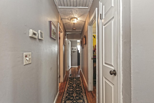 corridor with a textured ceiling, dark wood-style floors, visible vents, and baseboards