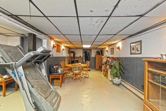 finished below grade area with a drop ceiling, a baseboard heating unit, and a wainscoted wall