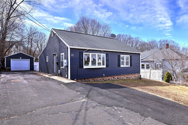 view of front of home with fence, roof with shingles, a detached garage, an outdoor structure, and aphalt driveway