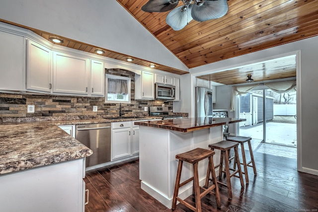 kitchen featuring a kitchen breakfast bar, tasteful backsplash, dark wood finished floors, stainless steel appliances, and wood ceiling