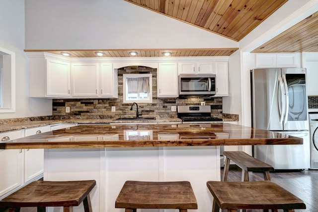 kitchen with decorative backsplash, vaulted ceiling, white cabinets, and stainless steel appliances