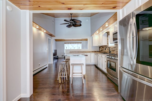 kitchen featuring tasteful backsplash, a baseboard heating unit, appliances with stainless steel finishes, a kitchen breakfast bar, and a sink