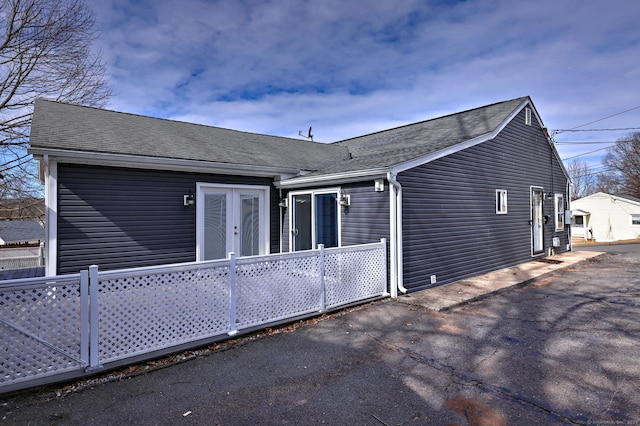 back of house with driveway, a shingled roof, french doors, and fence