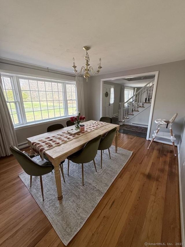 dining area featuring baseboard heating, a notable chandelier, wood finished floors, and stairs