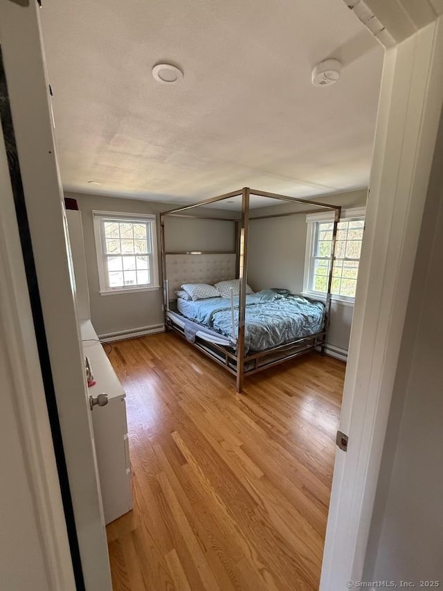 bedroom with a baseboard heating unit, light wood-type flooring, baseboards, and multiple windows