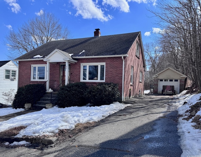 bungalow with a garage, a chimney, aphalt driveway, an outbuilding, and brick siding