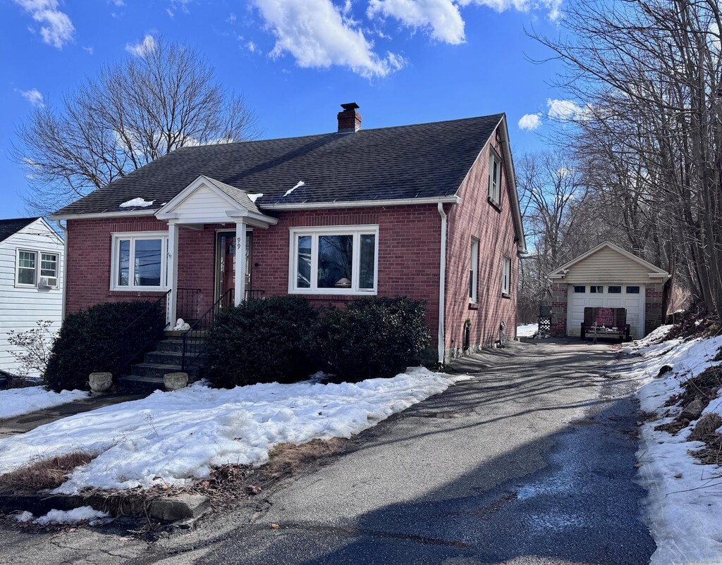 bungalow-style home featuring driveway, brick siding, an outdoor structure, and a chimney
